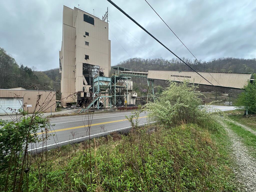 Roadside view of tall prep-plant tower with enclosed conveyor labeled ‘Bledsoe Coal Corp’ spanning the road.