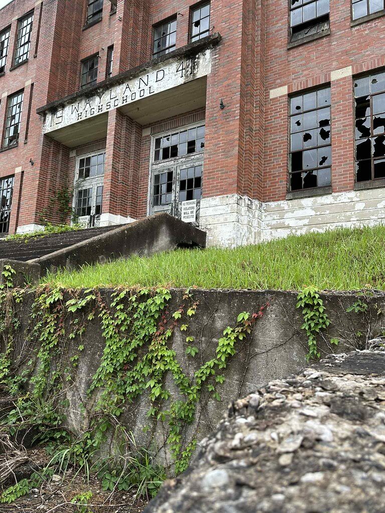 Front entrance of the former Wayland High School in Wayland, Kentucky, brick facade with broken windows and ivy-covered wall.