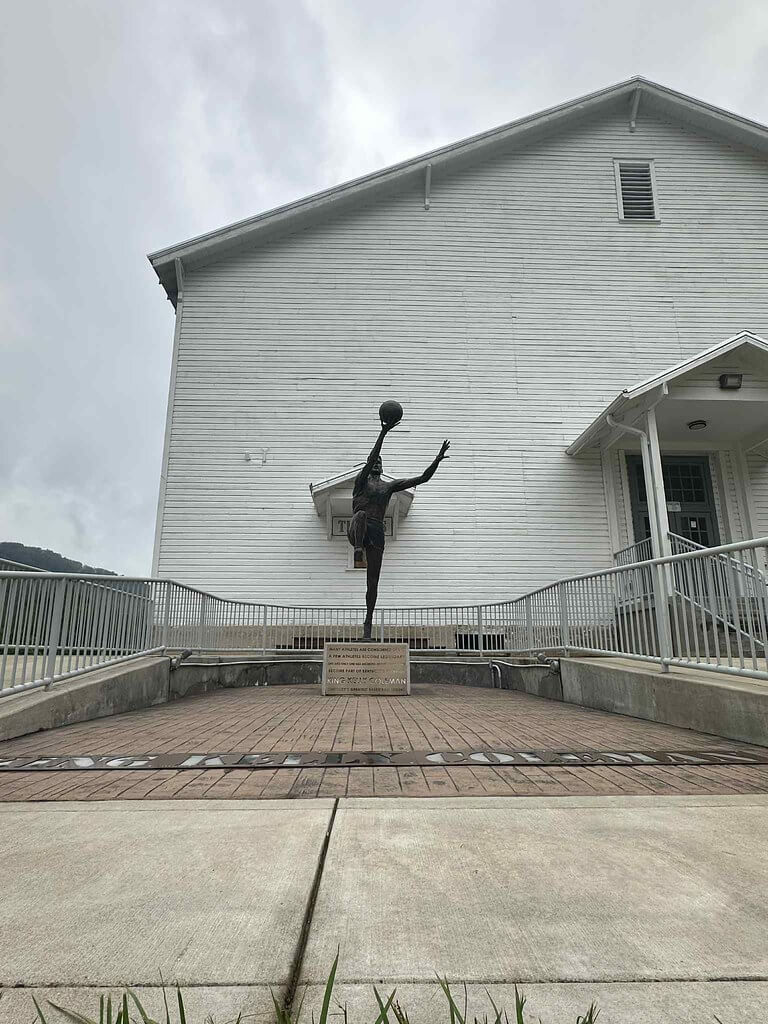 Bronze statue of Kelly “King” Coleman in a layup pose outside the restored white-clapboard Wayland gym and Mountain Sports Hall of Fame.