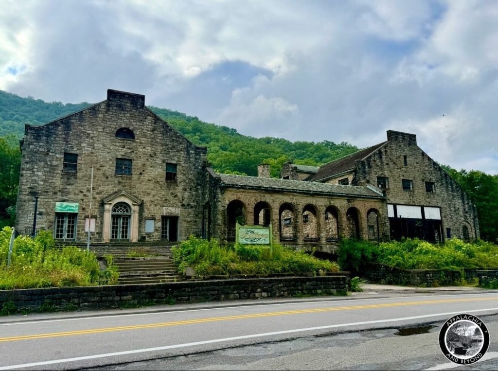 Wide roadside view of the Itmann Company Store and Office, twin gabled wings and arcaded courtyard against a green mountain slope.