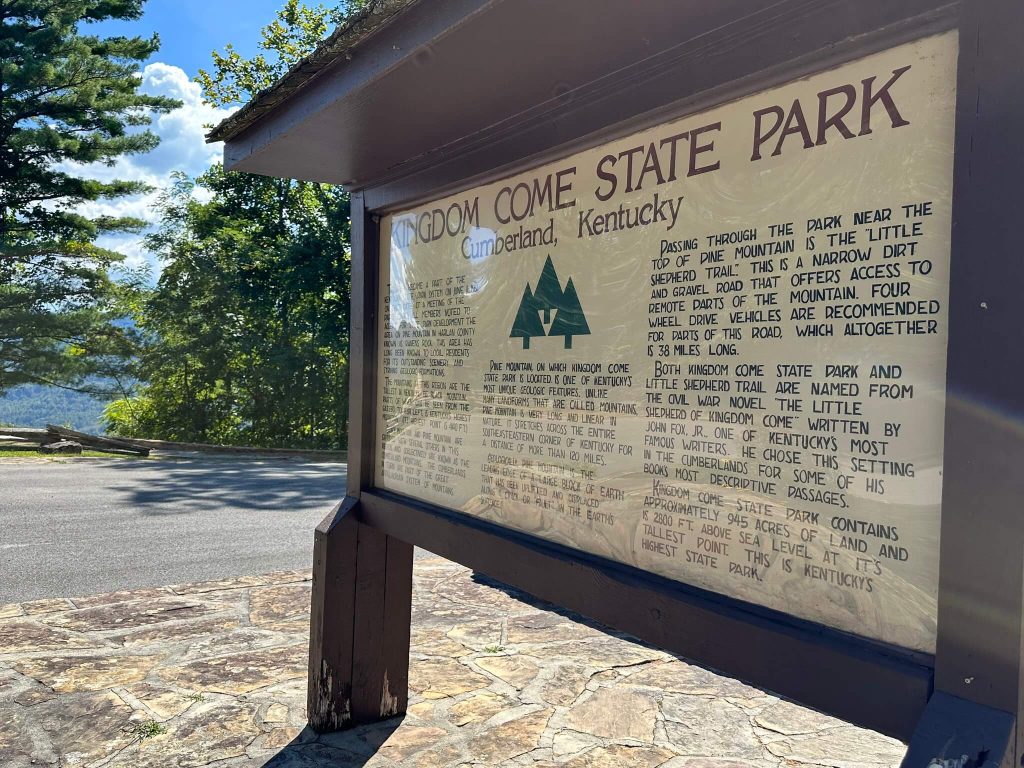 Stone pavilion at Kingdom Come State Park with a circular bench and central stone pillar under a dark wooden roof, looking out through open arches toward the surrounding forest.