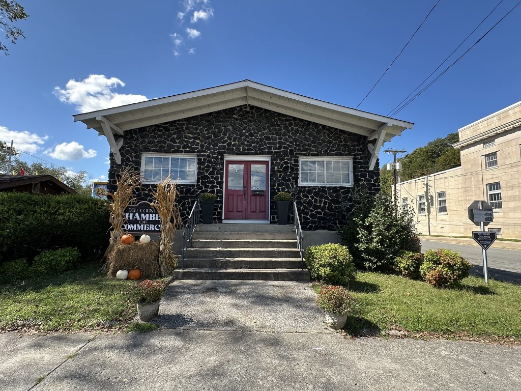 Front view of the Bell County Coal House, a one-story black stone building with a red double door, fall decorations of hay bales and pumpkins, and a sign reading “Bell County Chamber of Commerce” by the steps.