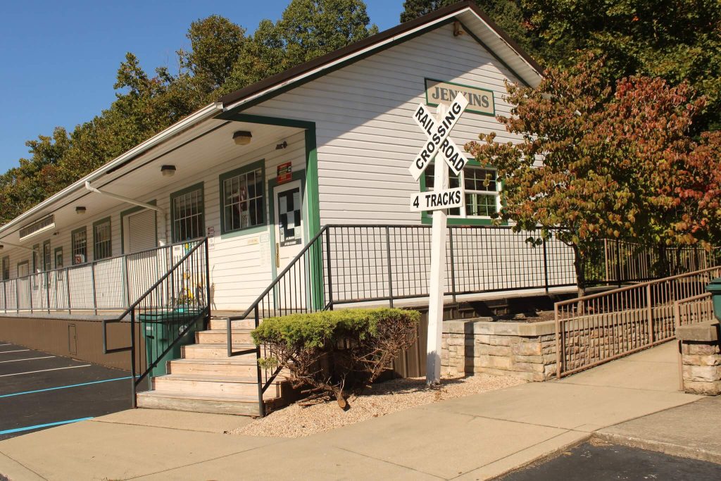 estored Jenkins Depot in Jenkins, Letcher County, Kentucky, with a “Railroad Crossing – 4 Tracks” sign beside the green-trimmed station building.