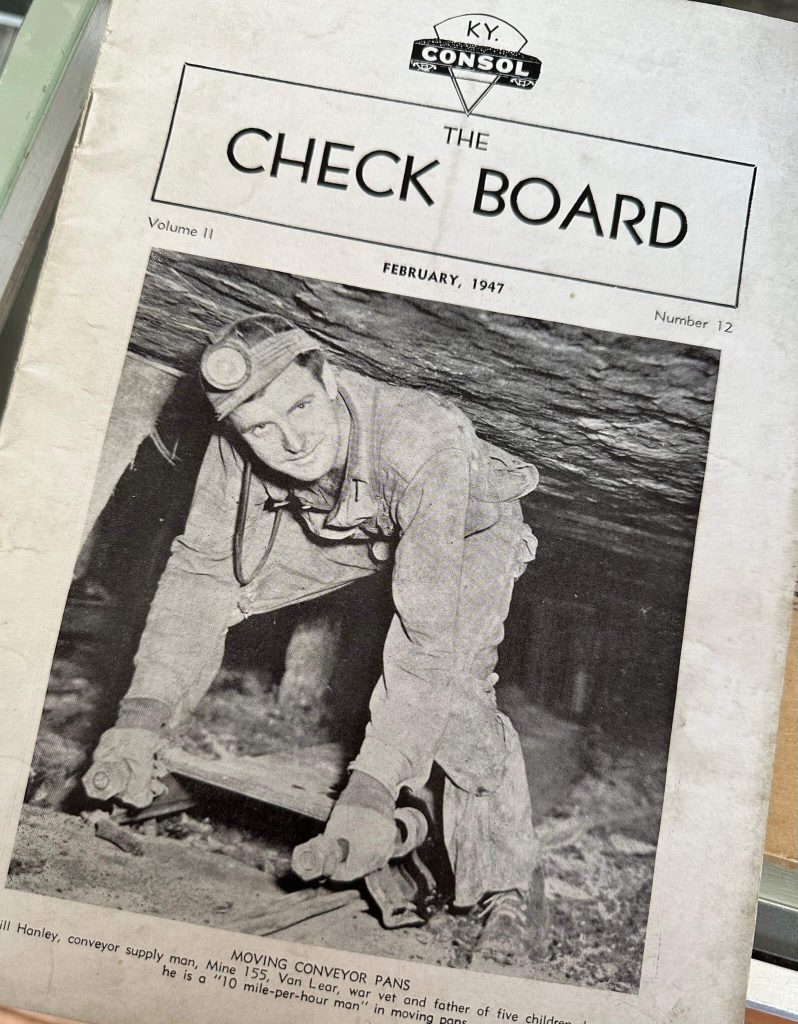 Close-up of “The Check Board” (KY Consol), February 1947, showing a miner underground with the caption “Moving Conveyor Pans.”