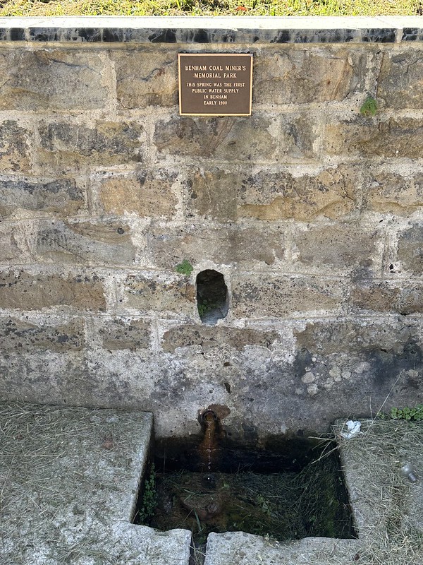 Stone spring box in Benham Coal Miners Memorial Park with a plaque noting Benham’s first public water supply.