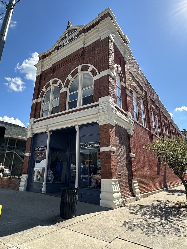 Low angle street view of the historic 1890 A.D. Campbell Building in Middlesboro, Kentucky, red brick with tall arched windows and a clothing storefront on the corner.