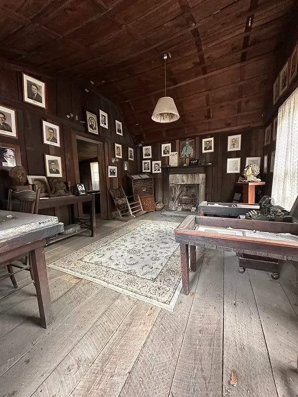 Interior of Founder’s Shack at Alice Lloyd College with wooden desks, portraits on dark plank walls, and a stone fireplace.